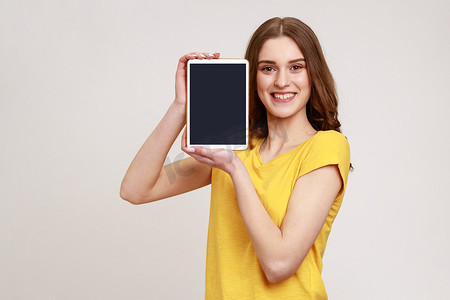 女孩播种摄影照片_美丽微笑的年轻青少年的肖像，棕色头发站立，拿着平板电脑空屏幕，播种设备，看着相机。
