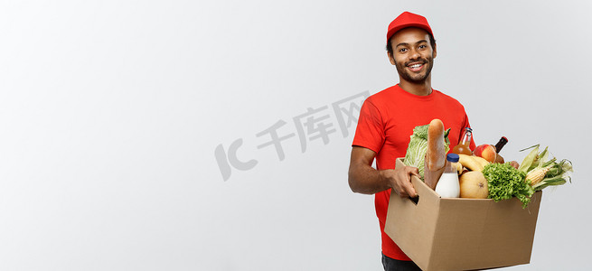 送货概念 — 英俊的非洲裔美国送货员从商店携带杂货食品和饮料的包装盒。