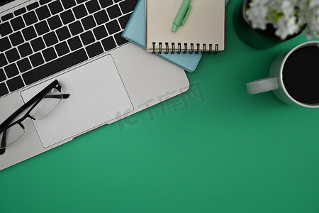 查看便签摄影照片_在绿色背景上查看电脑笔记本电脑、眼镜、笔记本和咖啡杯。