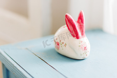 玫瑰兔子摄影照片_兔子陶瓷人物，鲜红色手绘耳朵和玫瑰