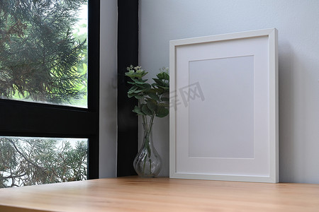 白色相框和盆栽植物放在靠近窗户的木桌上。