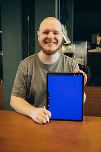 坐在现代咖啡馆附近的长椅上，快乐的男性用手指指着空白的平板电脑蓝屏