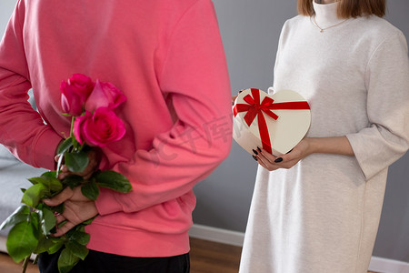 一个男人，背着一束玫瑰，一个女孩，拿着一个心形的白色盒子。