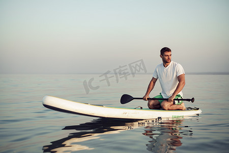 sup浆板摄影照片_穿着 T 恤和短裤的年轻人漂浮在 SUP 板上