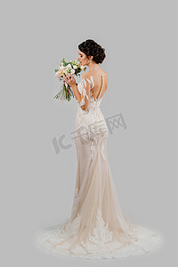 穿着婚纱的新娘在空白背景的工作室里举行和嗅探花束。