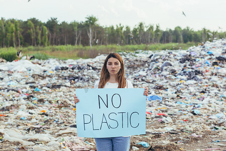 迎宾海报婚礼摄影照片_女志愿者在垃圾填埋场举着无塑料海报，积极分子与环境污染作斗争