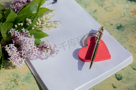 模拟关于爱情的信。红色的木心躺在一张木桌上的空白白纸上，上面放着春天的花朵，一张情人节贺卡，上面放着你的文字。