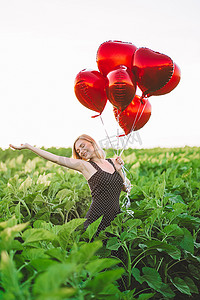 气球火箭摄影照片_穿着减速火箭的红色礼服的俏丽的妇女与在绿色领域的心形气球合影。