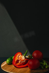 木板上鲜绿芦笋、辣椒、西红柿和黄瓜的枝条，深灰色背景，顶视图。