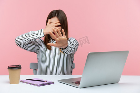不要生气摄影照片_情绪化的年轻女性坐在粉红色背景的办公室里工作。