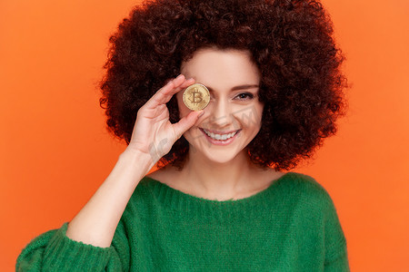 快乐微笑的女人的肖像，非洲发型，穿着绿色休闲风格毛衣，眼睛上覆盖着黄金比特币，区块链概念。