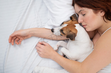 白人妇女抱着她心爱的狗在床上打盹。