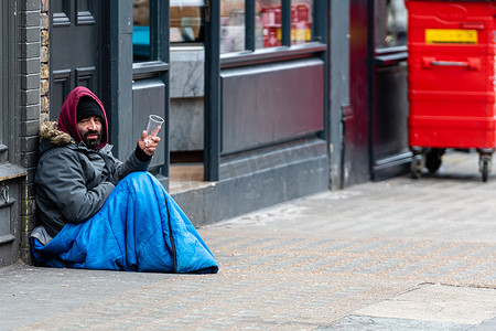 一个留着胡子的男子坐在人行道上向路人乞讨
