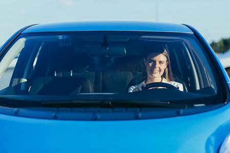 一位成功而幸福的女性驾驶汽车的肖像，从前面透过玻璃拍摄的照片
