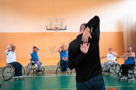 残疾篮球队的选拔员站在球员面前，为他们展示训练开始前的伸展运动
