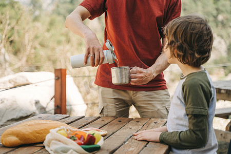 在山上的一次家庭野餐中，爸爸爸爸把热水瓶里的热咖啡茶倒进杯子里。