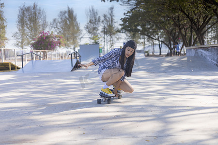 年轻的亚洲女性早上在户外的公园滑板坡道上玩冲浪滑板。