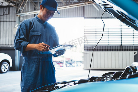 汽车修理工拿着剪贴板并根据客户索赔订单在汽车修理店车库检查维修车辆。
