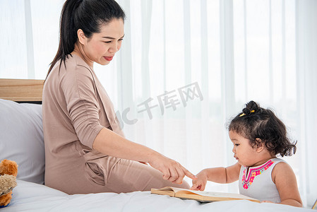 母亲读书摄影照片_亚洲母亲教女儿在家读书。