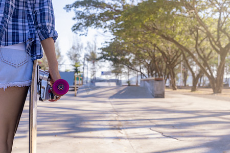 关闭年轻女性手持滑板，在公共滑板坡道公园背景上冲浪滑冰。