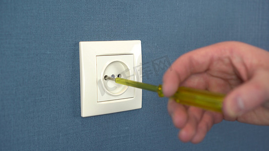 电工用专用螺丝刀拆开墙上的插座。
