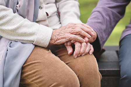 两手摄影照片_坐在公园长椅上的两位老年妇女手牵着快乐的长寿朋友享受退休生活