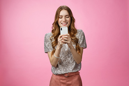 迷人的魅力、善于交际的时尚白人女性使用智能手机看手机屏幕看小工具显示有趣的写作后上传照片社交网页发短信，粉红色背景