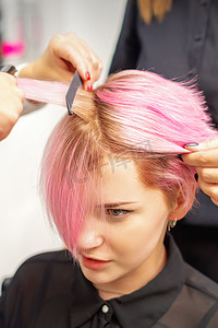 美发师用烫发器拉直女人的粉红色头发。