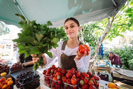 水果商店摄影照片_年轻女售货员在工作，手里拿着欧芹和西红柿