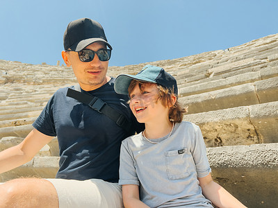 年轻的父亲和他的小学生儿子游客在炎热的夏日参观古代古董竞技场圆形剧场遗址