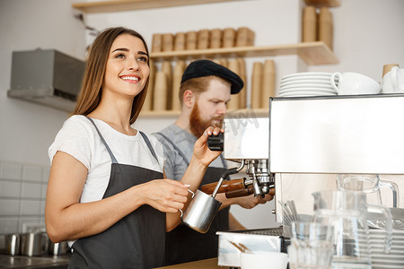 咖啡馆摄影照片_咖啡业务概念-站在咖啡馆时，女咖啡师穿着围裙准备和蒸牛奶，与她的伴侣一起点咖啡。