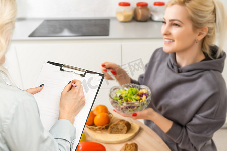 饮食计划摄影照片_女营养师老师就饮食健康提出建议定义饮食工作厨房工作室饮食计划医疗减肥或视频通话感兴趣的人并在直播中在线咨询。