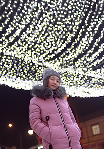 市中心的女人带着圣诞灯、天空节日的灯光闪耀和发光、散焦图像
