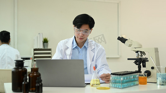 报告总结摄影照片_年轻男性生物化学家使用笔记本电脑，收集数据并总结科学报告的信息