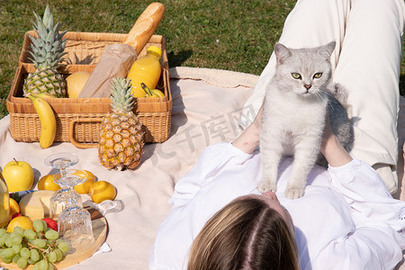 一位身穿白衬衫的年轻女子正带着她的宠物小猫在野餐时休息，