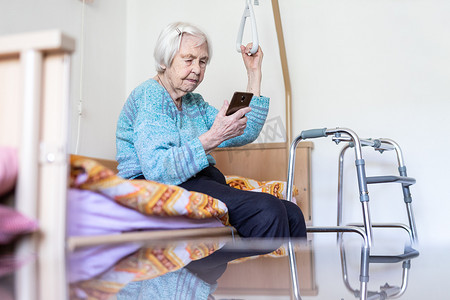 96 岁的老妇坐在医疗床上，由持有人扶着她阅读电话留言。