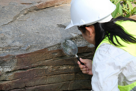 亚洲女地质学家研究员在自然公园用放大镜分析岩石。