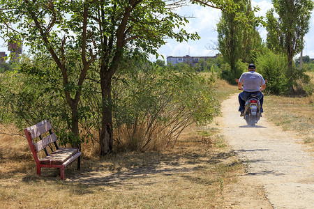居民生活摄影照片_乡村静物，有一条旧长凳、骑摩托车的居民和一条旧路。
