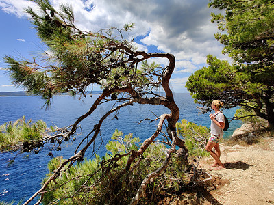 年轻活跃的女性游客穿着小背包，在松树间的沿海小路上行走，寻找偏远的海湾，在克罗地亚的海边和平地独自游泳。