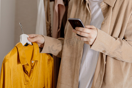 女人拿着智能手机给她的旧衣服拍照，然后在网上卖。