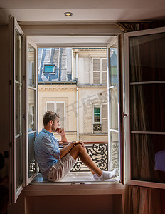 法国的卧室摄影照片_年轻人坐在窗前，眺望巴黎这座城市。