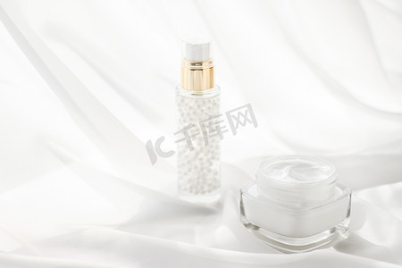 白丝绸上的面霜保湿罐和血清凝胶、护肤乳液和提升乳液、豪华美容护肤品牌的抗衰老化妆品