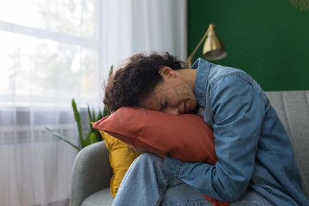 暴风哭泣摄影照片_家里的女人坐在沙发上抱着枕头哭泣，西班牙裔女人在家郁闷