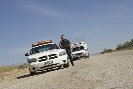 警察在巡逻车上使用 CB 无线电的全长，背景是救护车