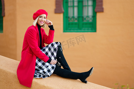 坐在古老彩色建筑附近边界上的时尚快乐女人