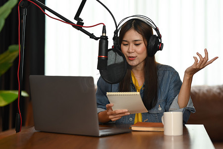 在小房子工作室使用麦克风和笔记本电脑录制播客的微笑亚洲女电台主持人