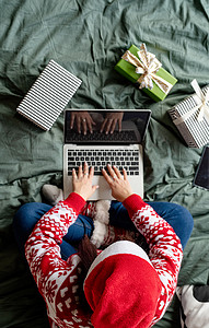 圣诞衣服摄影照片_穿着圣诞衣服的女人坐在床上用笔记本电脑