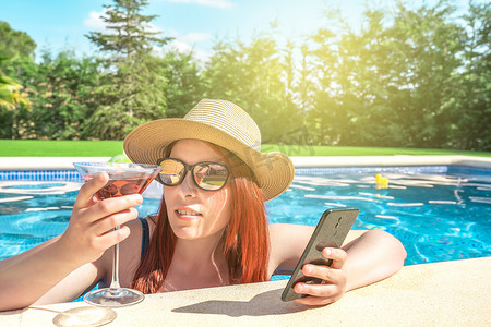 年轻女子在泳池内放松，看着她的手机。