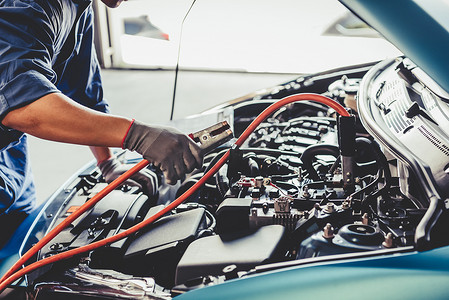 汽车修理工通过电缆跨接器保持电池电力，并根据客户索赔订单在汽车修理厂车库检查维修车辆。