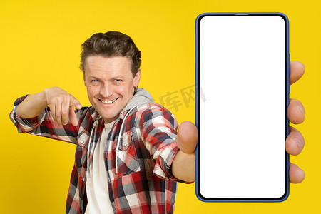 大屏展台摄影照片_身穿红色格子衬衫的白屏金发白人男子指着手中的大智能手机。